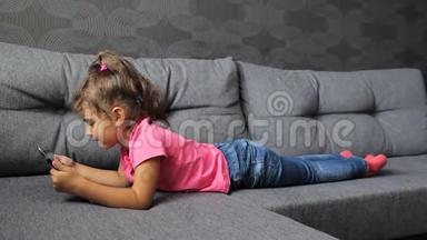 小女孩躺在沙发上用平板电脑。 小女孩躺着玩平板电脑